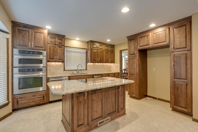 kitchen with appliances with stainless steel finishes, backsplash, light stone counters, sink, and a center island