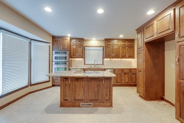 kitchen with light stone countertops, a center island, sink, stainless steel double oven, and decorative backsplash