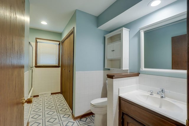 bathroom with tile patterned floors, walk in shower, vanity, tile walls, and toilet