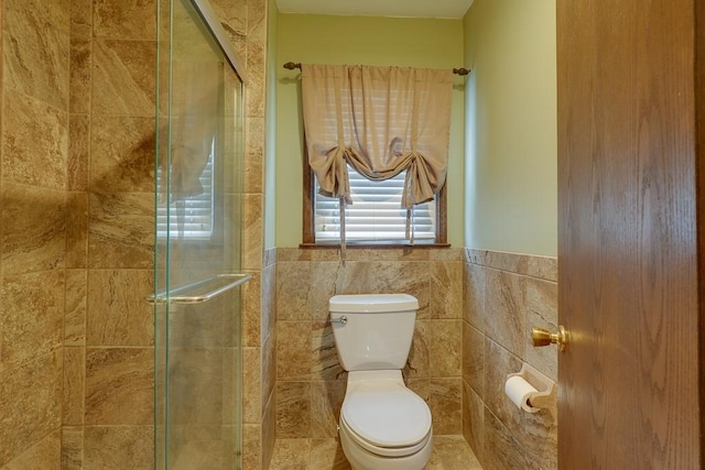 bathroom with a shower with door, tile walls, and toilet