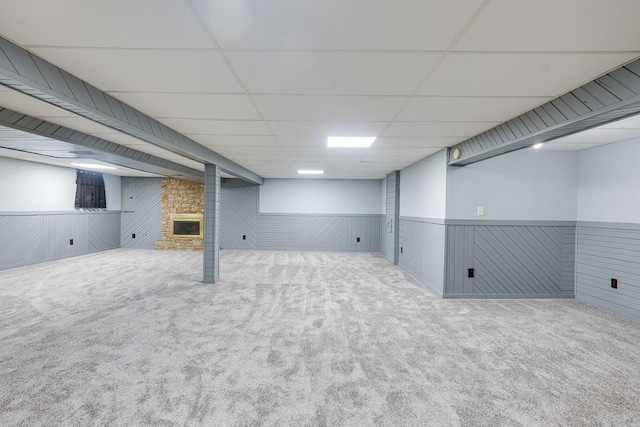 basement with wooden walls, a large fireplace, carpet floors, and a paneled ceiling