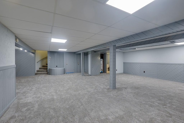 basement with wood walls, a drop ceiling, and carpet