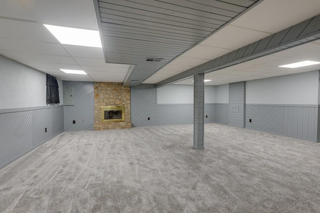 basement featuring carpet flooring, a paneled ceiling, wood walls, and a fireplace