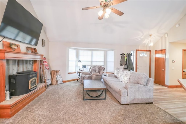 carpeted living room featuring a wood stove, ceiling fan, and lofted ceiling