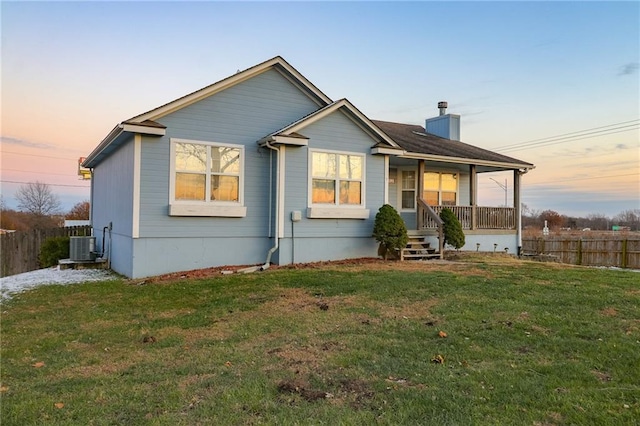 back house at dusk with covered porch, a yard, and cooling unit