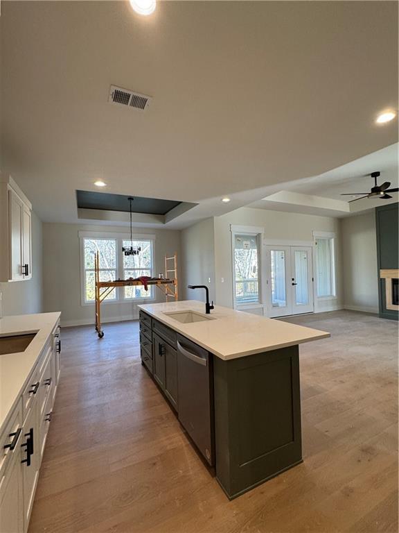 kitchen featuring white cabinets, light hardwood / wood-style floors, stainless steel dishwasher, and an island with sink