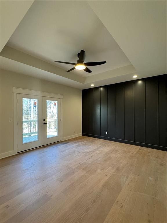 empty room featuring french doors, a tray ceiling, light hardwood / wood-style flooring, and ceiling fan