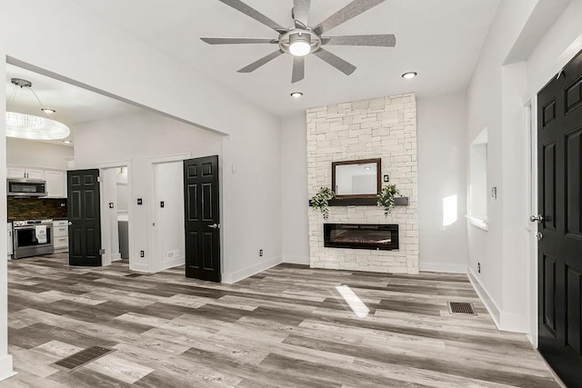 unfurnished living room featuring hardwood / wood-style floors, ceiling fan, and a stone fireplace