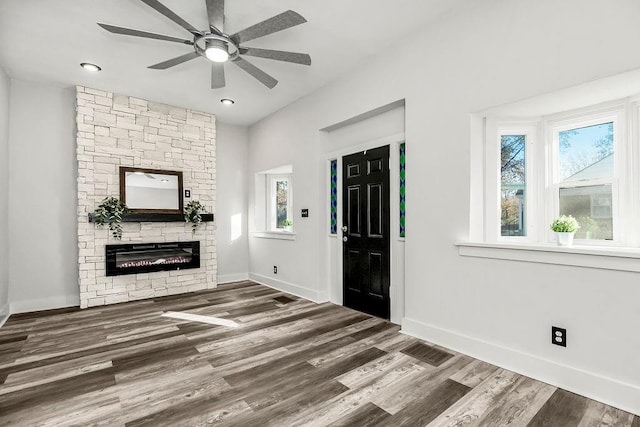 entrance foyer featuring ceiling fan, a healthy amount of sunlight, a stone fireplace, and dark wood-type flooring