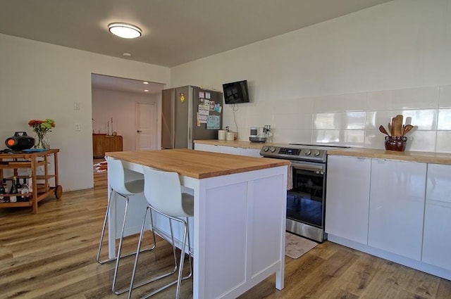 kitchen featuring wooden counters, a kitchen breakfast bar, stainless steel appliances, a kitchen island, and white cabinetry