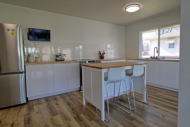 kitchen with wooden counters, appliances with stainless steel finishes, a kitchen island, a kitchen bar, and white cabinetry