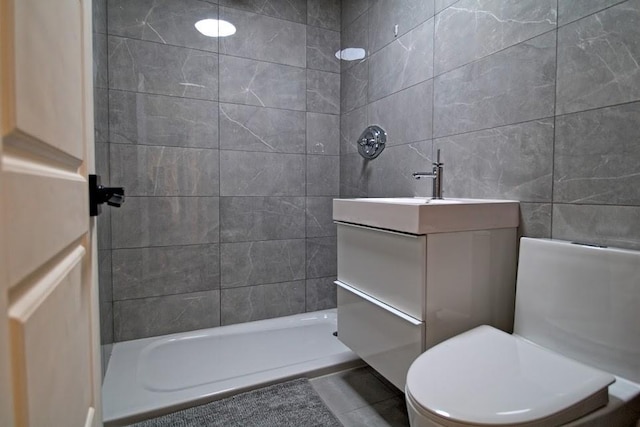 bathroom featuring tile patterned floors, toilet, tiled shower, vanity, and tile walls