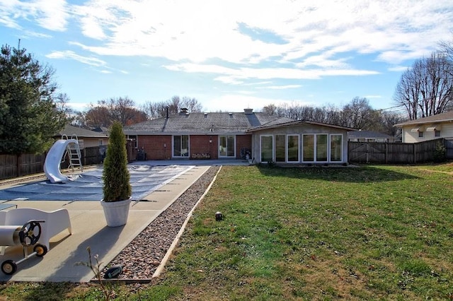 back of house with a sunroom, a patio area, a lawn, and a covered pool