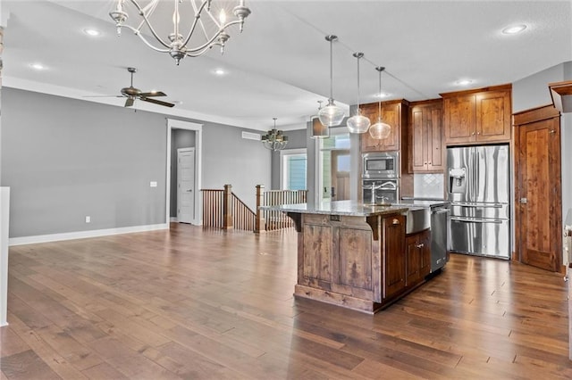 kitchen featuring dark wood-type flooring, light stone countertops, an island with sink, decorative light fixtures, and stainless steel appliances