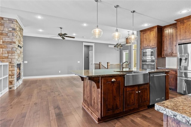 kitchen with pendant lighting, dark wood-type flooring, sink, an island with sink, and appliances with stainless steel finishes