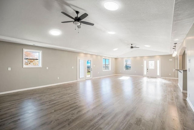 unfurnished living room featuring arched walkways, a healthy amount of sunlight, and wood finished floors