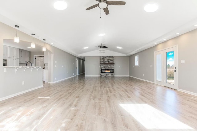 unfurnished living room featuring light wood-style flooring, a ceiling fan, vaulted ceiling, a stone fireplace, and baseboards