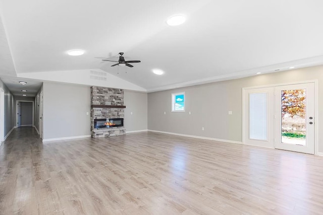 unfurnished living room with light wood finished floors, baseboards, lofted ceiling, ceiling fan, and a stone fireplace