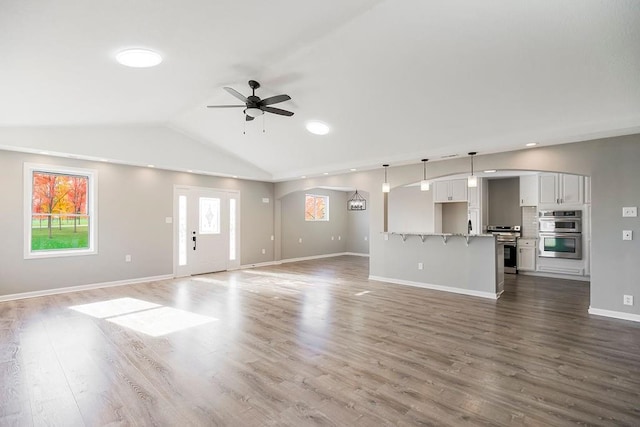 unfurnished living room with a ceiling fan, plenty of natural light, vaulted ceiling, and wood finished floors