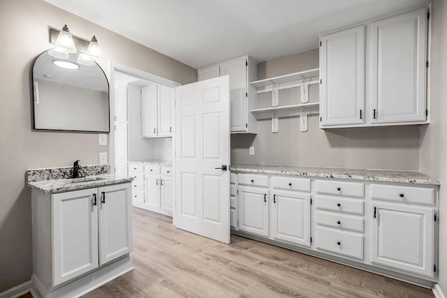 kitchen featuring white cabinetry, a sink, light wood finished floors, and light stone countertops