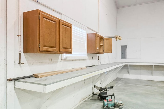 kitchen featuring brown cabinetry, light countertops, electric panel, and concrete flooring