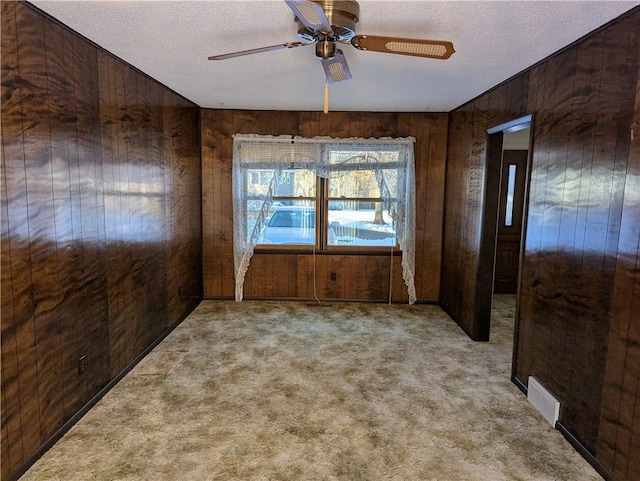 carpeted empty room with a textured ceiling, ceiling fan, and wood walls