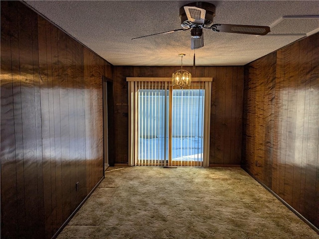 carpeted spare room featuring a textured ceiling, wooden walls, and ceiling fan with notable chandelier