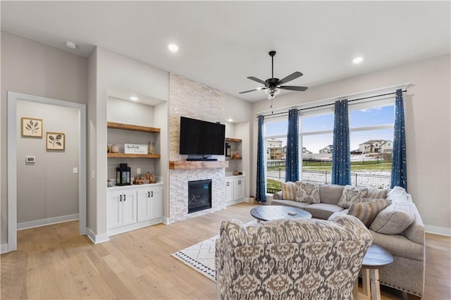 living room featuring ceiling fan, a stone fireplace, and light hardwood / wood-style flooring