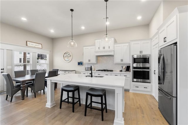 kitchen with white cabinets, appliances with stainless steel finishes, light hardwood / wood-style floors, and hanging light fixtures