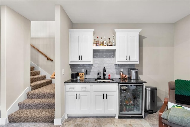 bar featuring sink, beverage cooler, dark stone countertops, decorative backsplash, and white cabinets