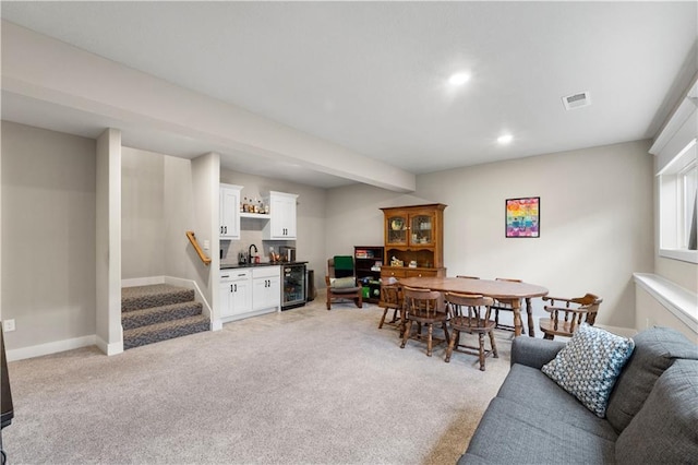 carpeted dining room with beam ceiling, wet bar, and beverage cooler