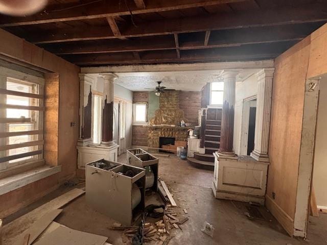 misc room with decorative columns, a stone fireplace, and ceiling fan