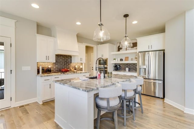 kitchen with a center island with sink, appliances with stainless steel finishes, custom range hood, pendant lighting, and white cabinets