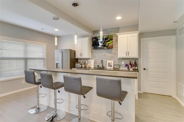 kitchen featuring tasteful backsplash, decorative light fixtures, a kitchen breakfast bar, stainless steel fridge, and white cabinets