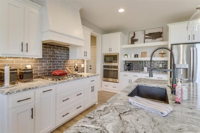 kitchen featuring sink, custom exhaust hood, light stone counters, appliances with stainless steel finishes, and white cabinets