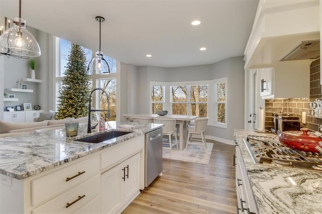 kitchen with sink, a kitchen island with sink, stainless steel appliances, white cabinets, and decorative light fixtures