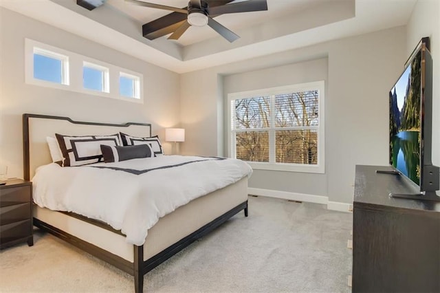 bedroom with light carpet, ceiling fan, and a tray ceiling