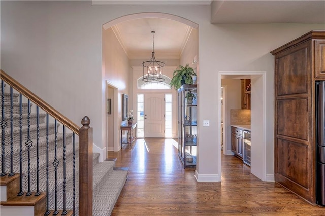 foyer entrance featuring dark wood-type flooring, an inviting chandelier, wine cooler, crown molding, and a towering ceiling