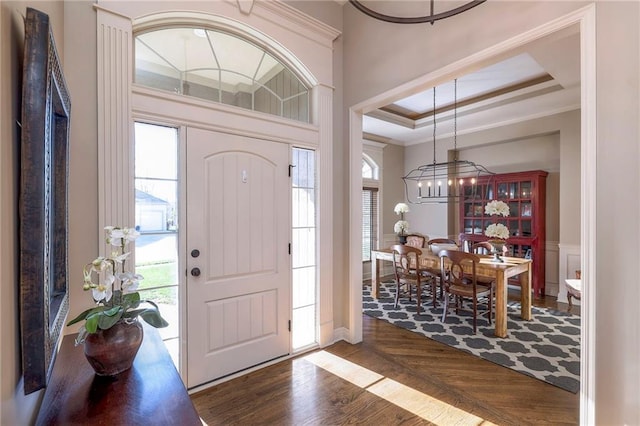 foyer featuring a notable chandelier, a raised ceiling, ornamental molding, and dark wood-type flooring