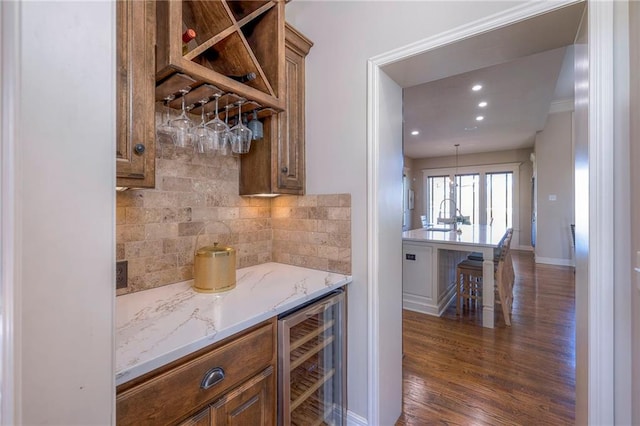 bar with backsplash, light stone counters, dark wood-type flooring, pendant lighting, and wine cooler