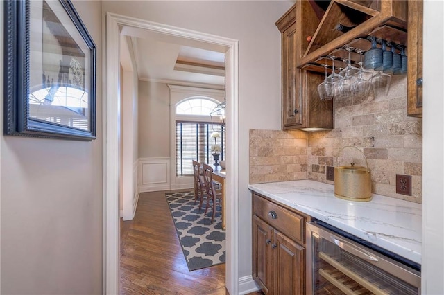 bar featuring dark wood-type flooring, a raised ceiling, light stone countertops, tasteful backsplash, and beverage cooler