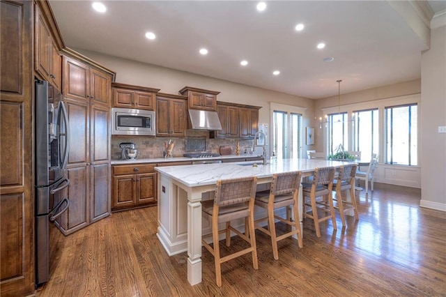 kitchen with a large island with sink, decorative backsplash, appliances with stainless steel finishes, decorative light fixtures, and a breakfast bar area