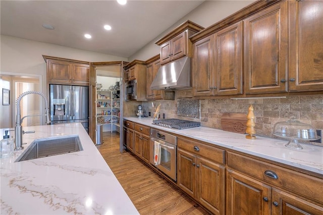 kitchen with appliances with stainless steel finishes, tasteful backsplash, light stone counters, sink, and light hardwood / wood-style flooring