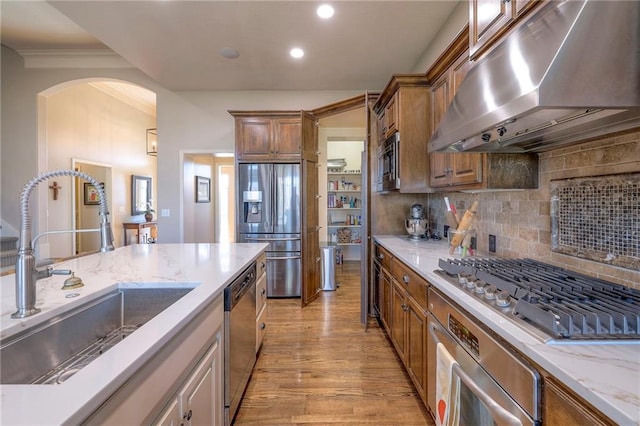 kitchen with sink, light hardwood / wood-style flooring, appliances with stainless steel finishes, tasteful backsplash, and extractor fan