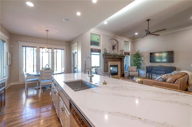 kitchen with light stone countertops, sink, dishwasher, hanging light fixtures, and dark hardwood / wood-style flooring