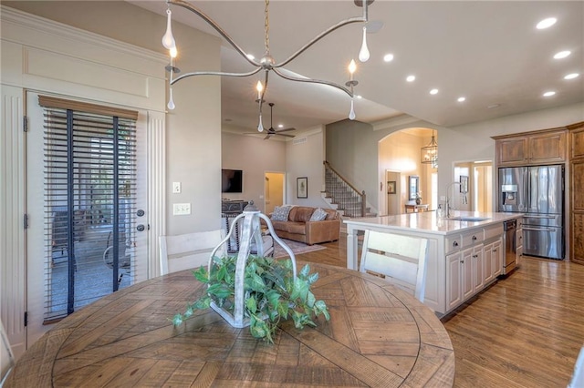 kitchen featuring stainless steel refrigerator with ice dispenser, ceiling fan with notable chandelier, sink, a center island with sink, and light hardwood / wood-style floors