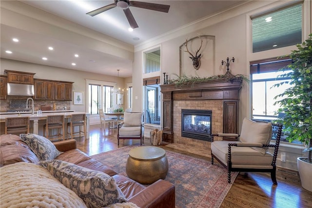 living room featuring sink, dark hardwood / wood-style flooring, crown molding, a fireplace, and ceiling fan with notable chandelier