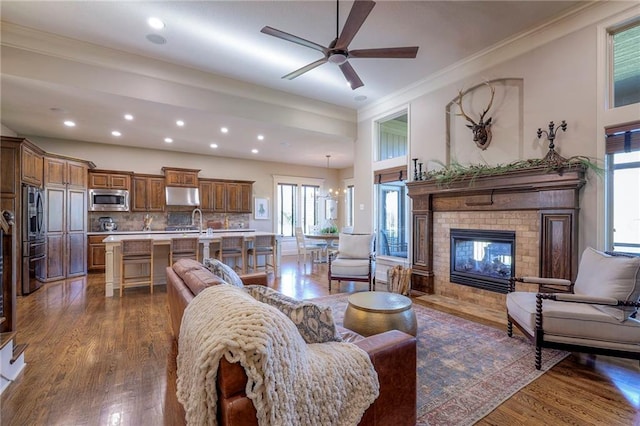 living room with ceiling fan, sink, dark wood-type flooring, a brick fireplace, and ornamental molding