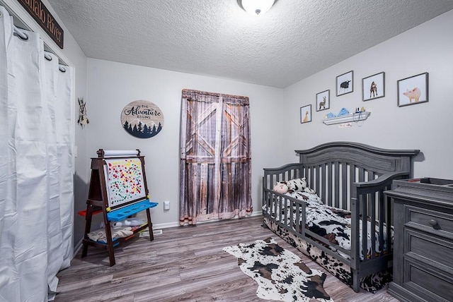 bedroom with a crib, a textured ceiling, and hardwood / wood-style flooring