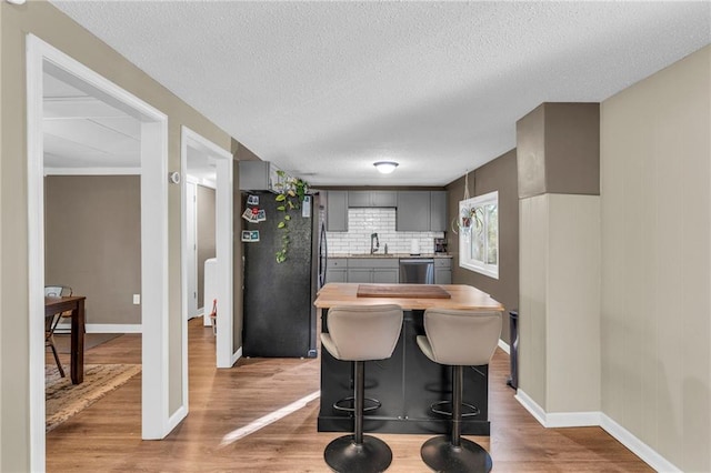 kitchen featuring gray cabinetry, black refrigerator, stainless steel dishwasher, decorative backsplash, and light hardwood / wood-style floors